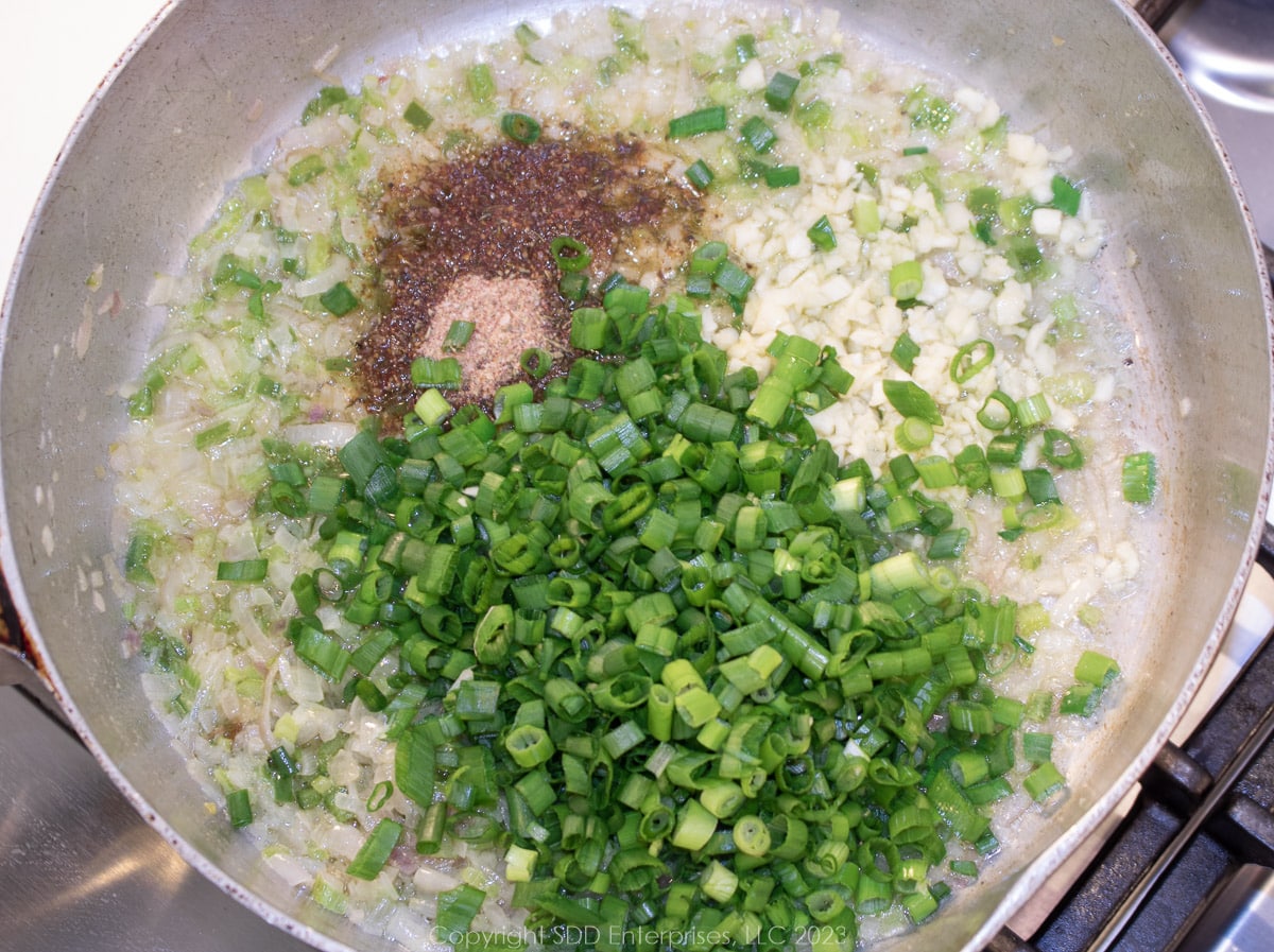herbs and spice and green onions added to the trinity on a frying pan