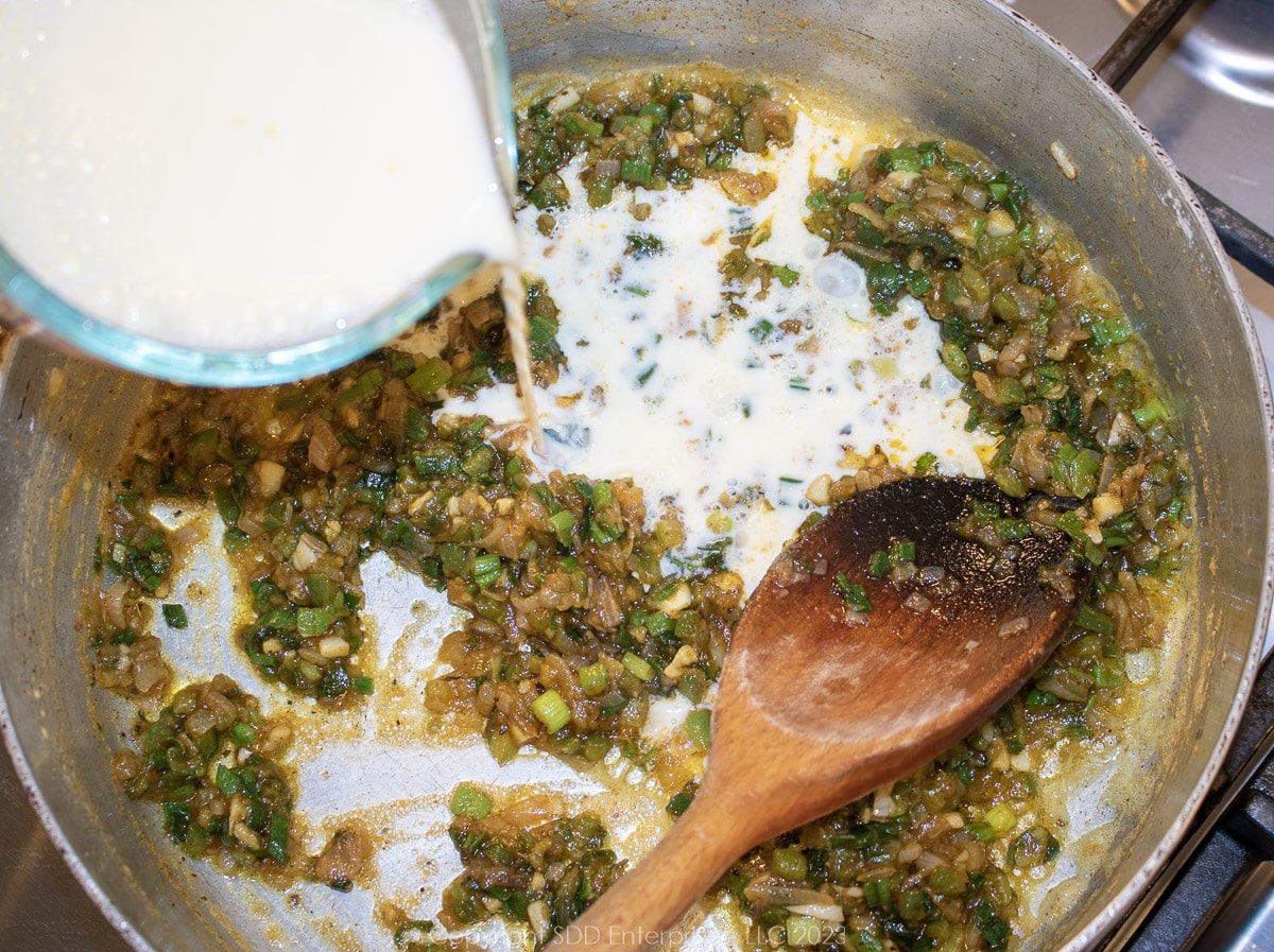 adding heavy cream to the roux and vegetables in a frying pan