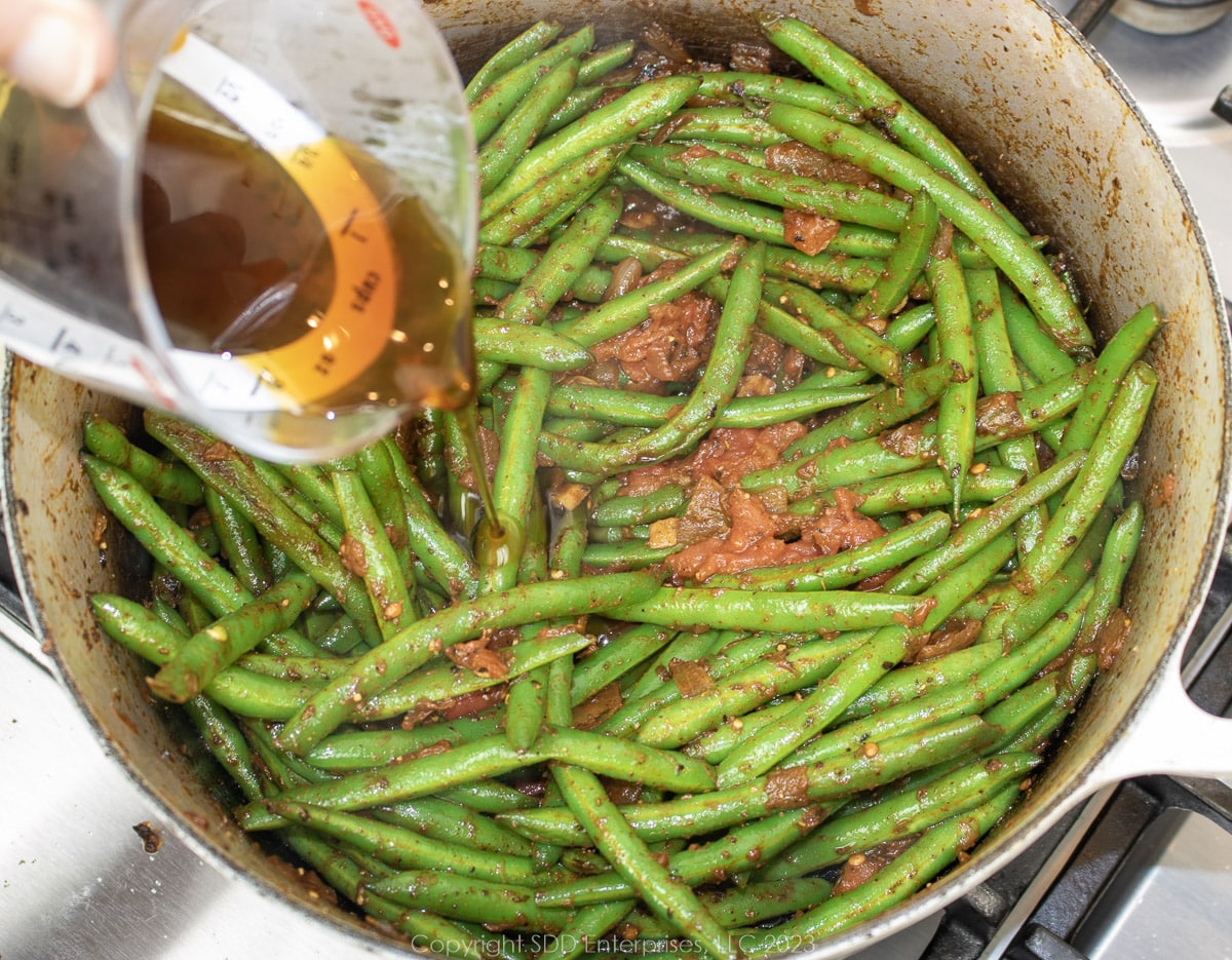 pouring cane syrup into simmering green beans in a Dutch oven