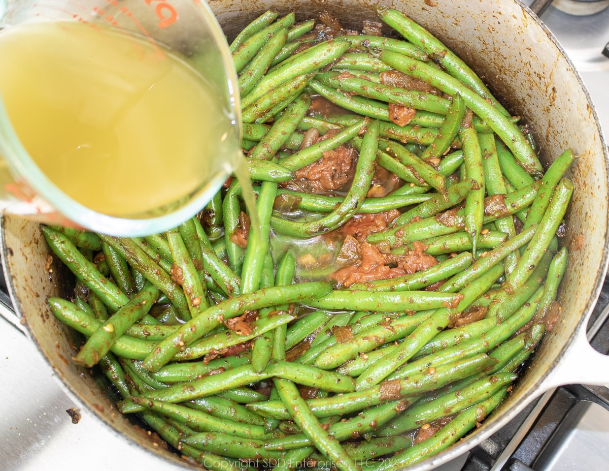 adding stock to green beans simmering in a Dutch oven