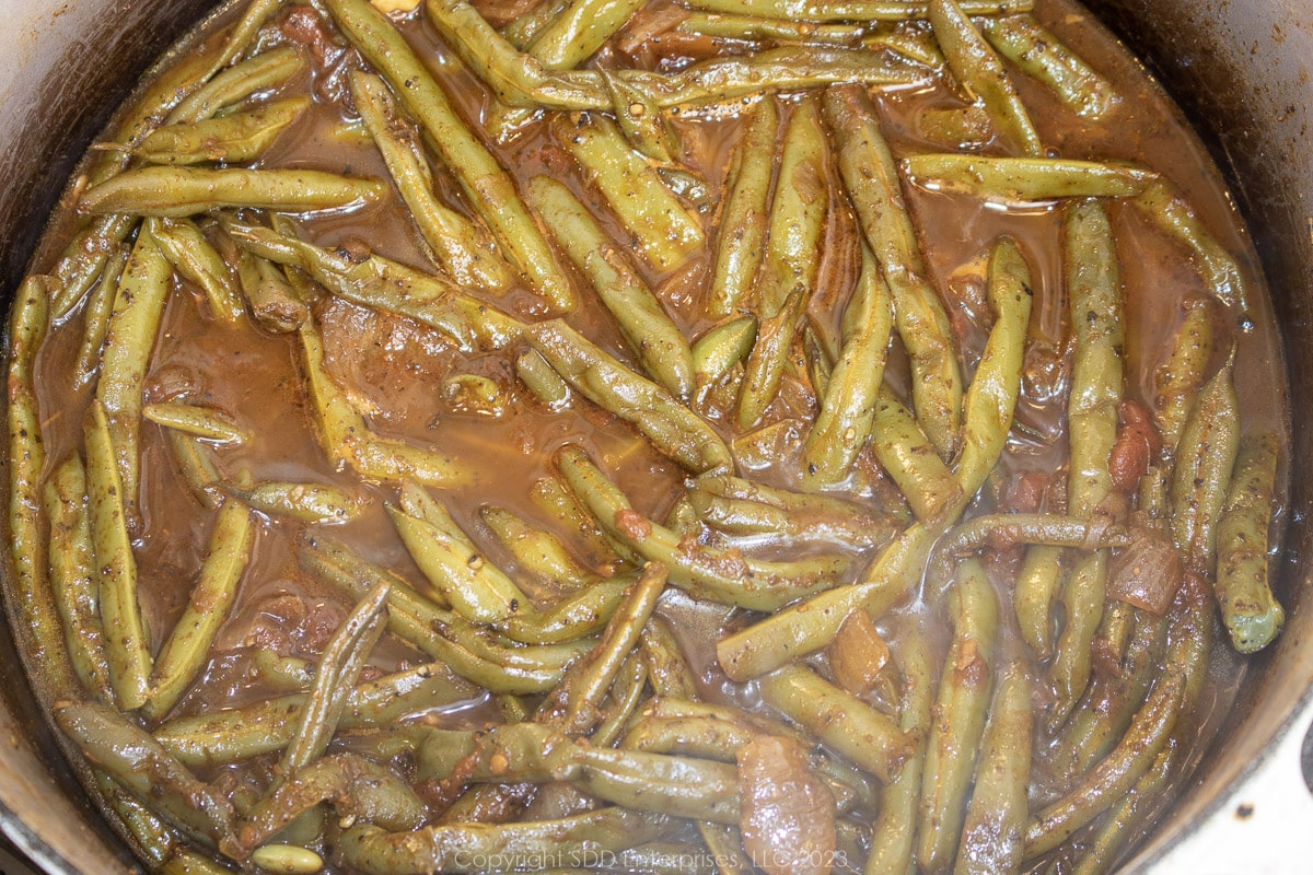 green beans and tomatoes simmering in seasoning and stock in a Dutch oven