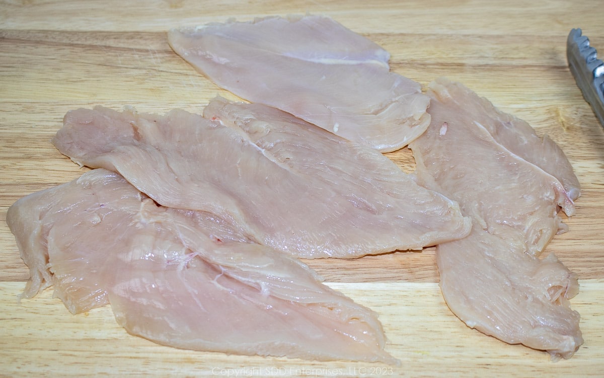 thinly sliced chicken breasts on a cutting board