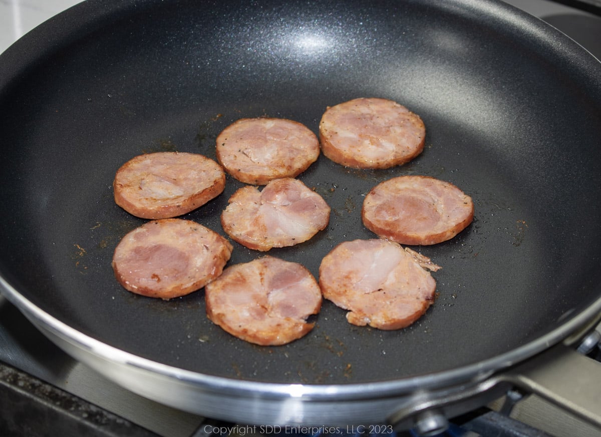 slices of andouille sausage browning in a fry pan