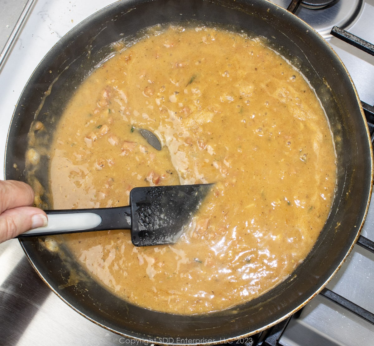 Stock and sherry with seasonings added to a roux in a saute pan