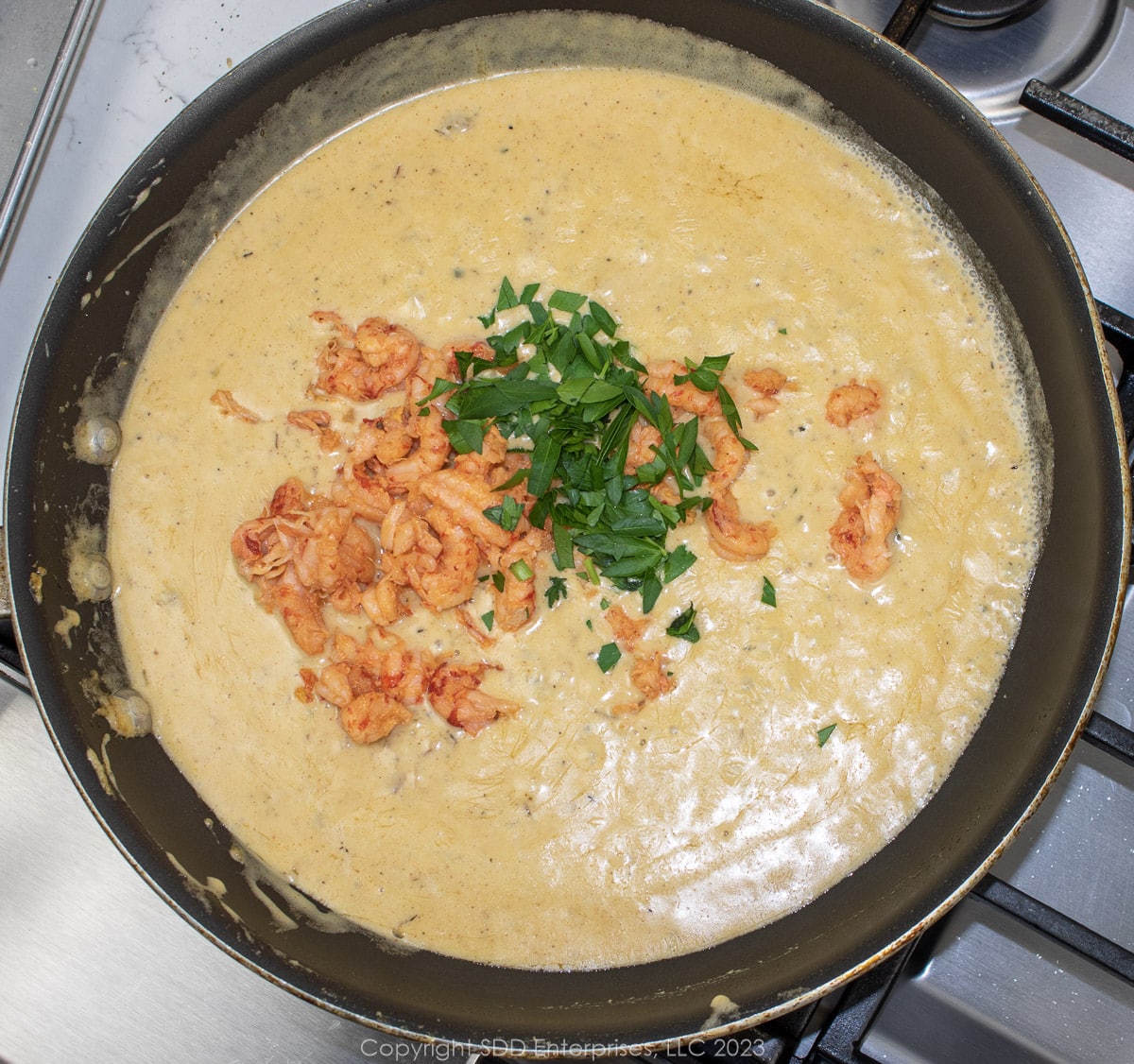 crawfish tails and parsley added to a cream sauce in a saute pan