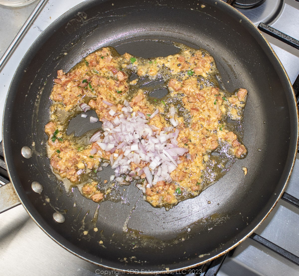 shallots added to compound butter and andouille in a saute pan