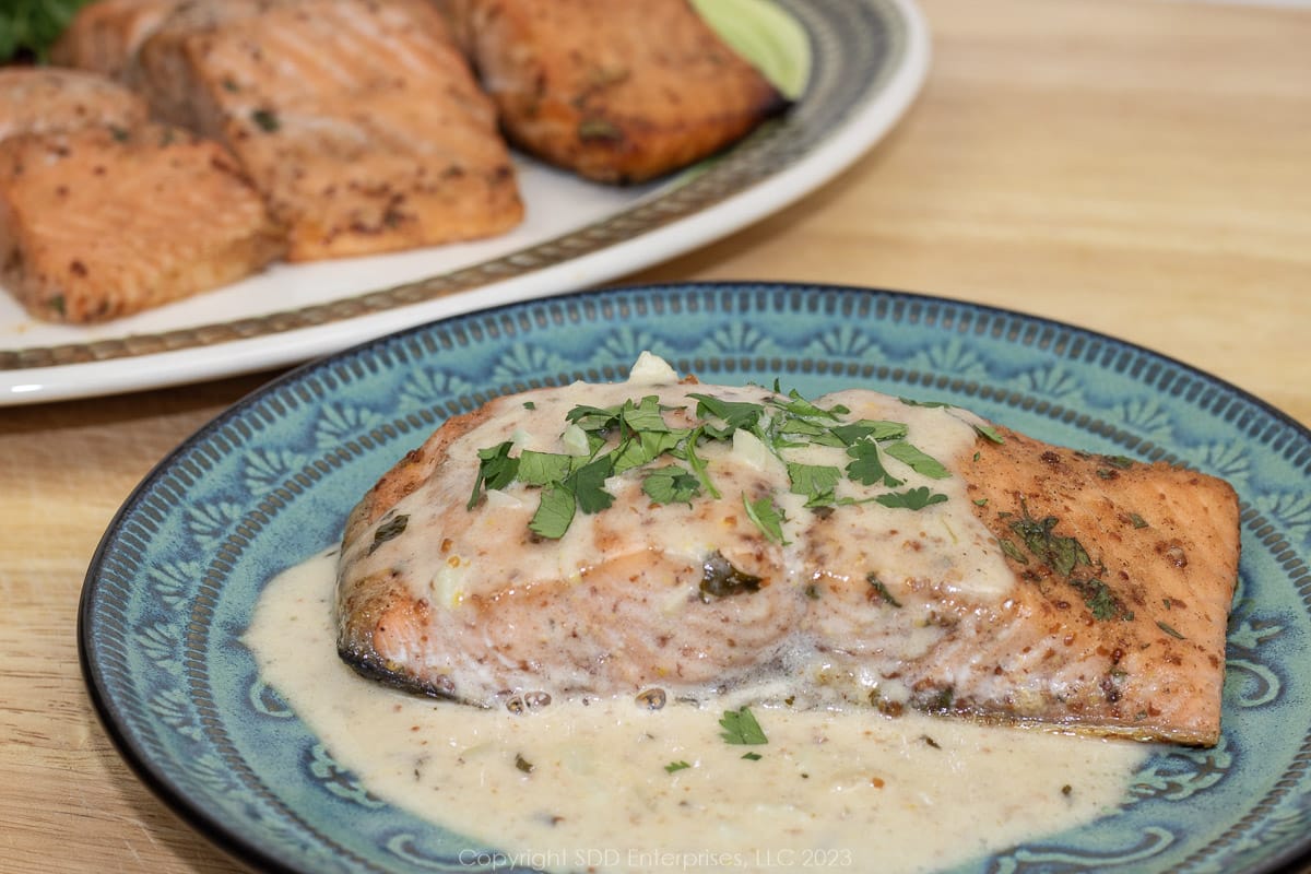 salmon with creamy sauce on a green plate with a platter of salmon on the side.