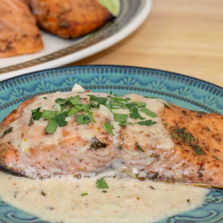 Baked salmon with Creole Mustards Cream Sauce on a blue green plate with platter in background