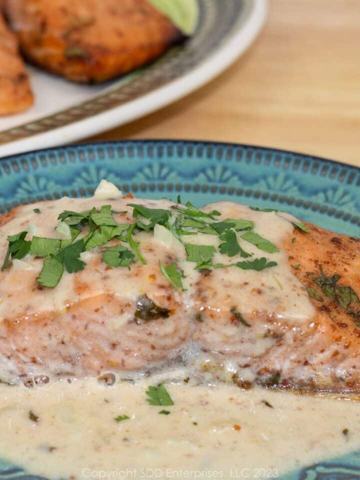 Baked salmon with Creole Mustards Cream Sauce on a blue green plate with platter in background
