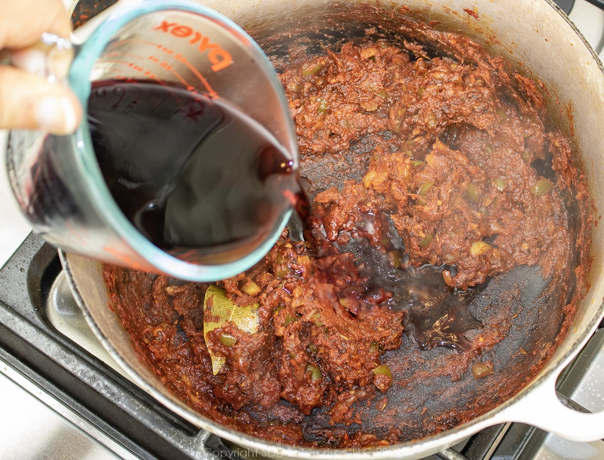 pouring red wine into the tomato paste in a Dutch oven