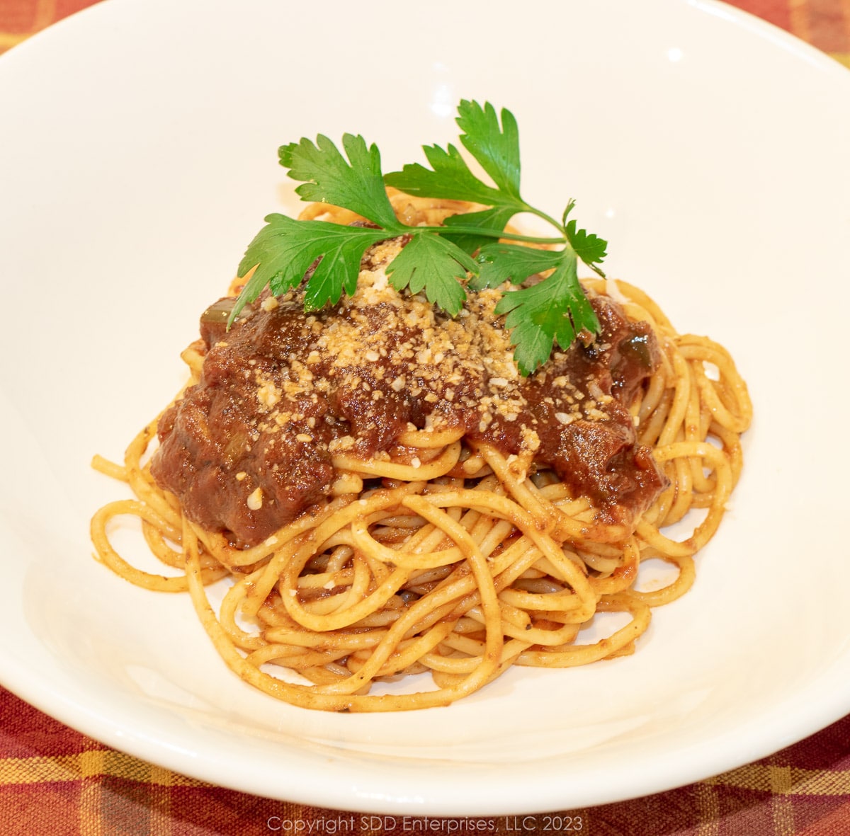 spaghettis noodles with Red Gravy in a white bowl with garnish