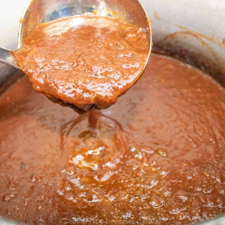 Italian red tomato gravy on a ladle over a Dutch oven