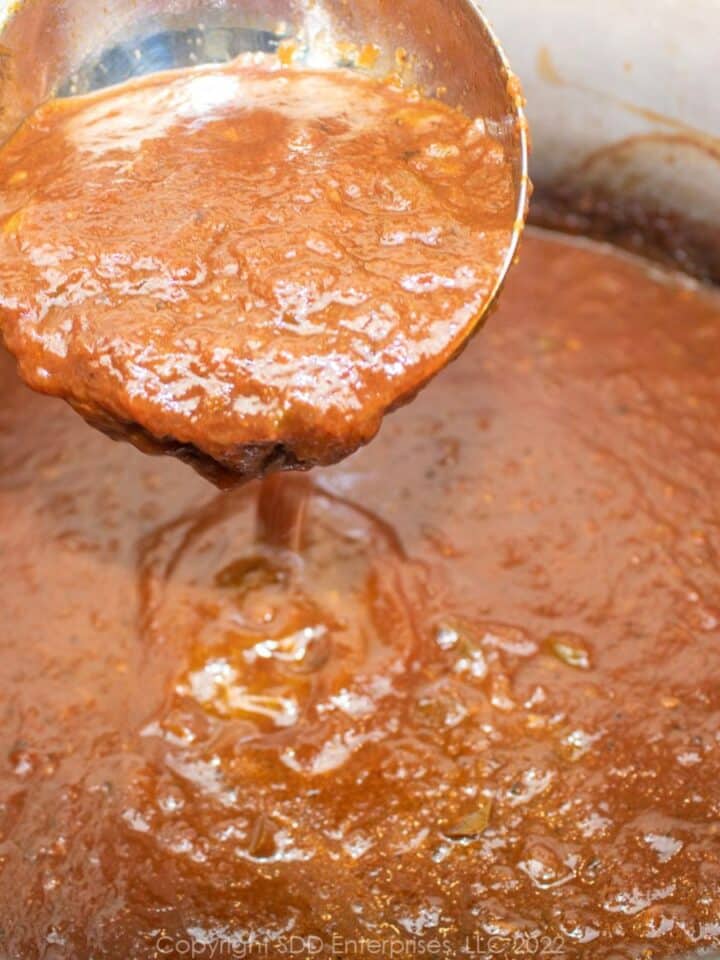 Italian red tomato gravy on a ladle over a Dutch oven