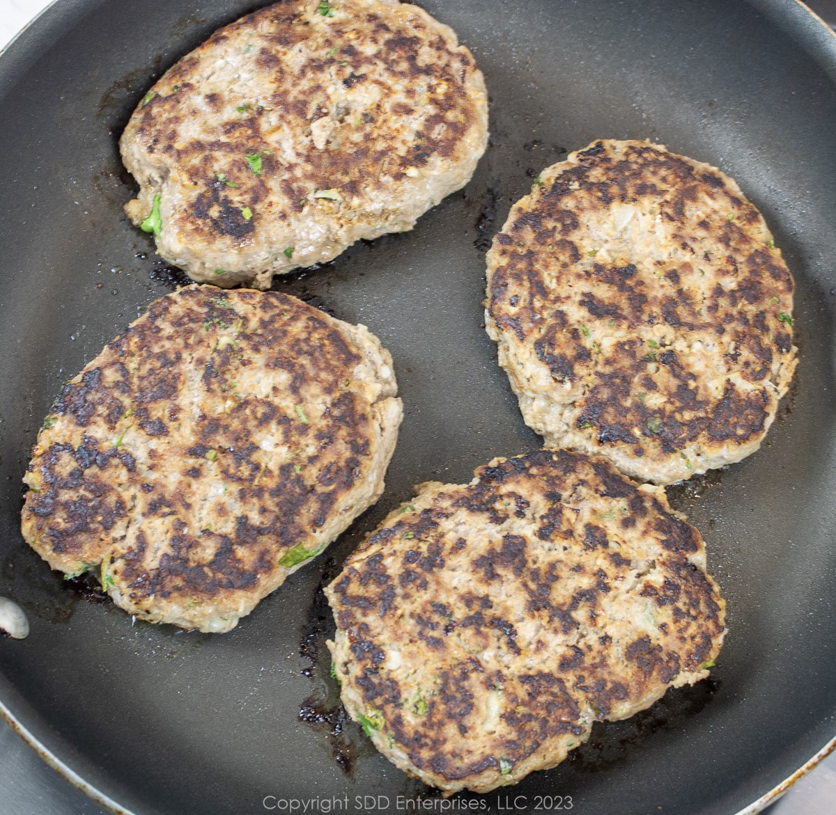 four Salisbury steak patties in a frying pan