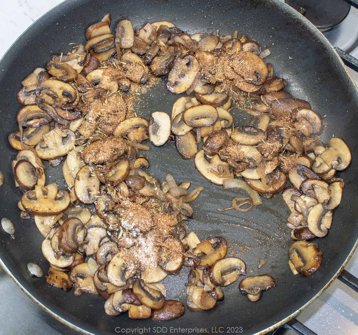 seasonings added to mushrooms on a frying pan