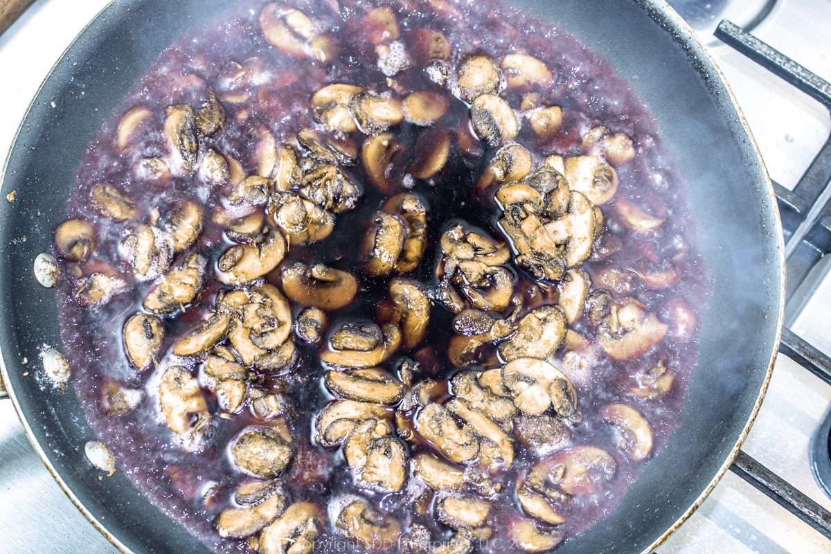 red wine added to sautéed seasoned mushrooms and roux in a frying pan