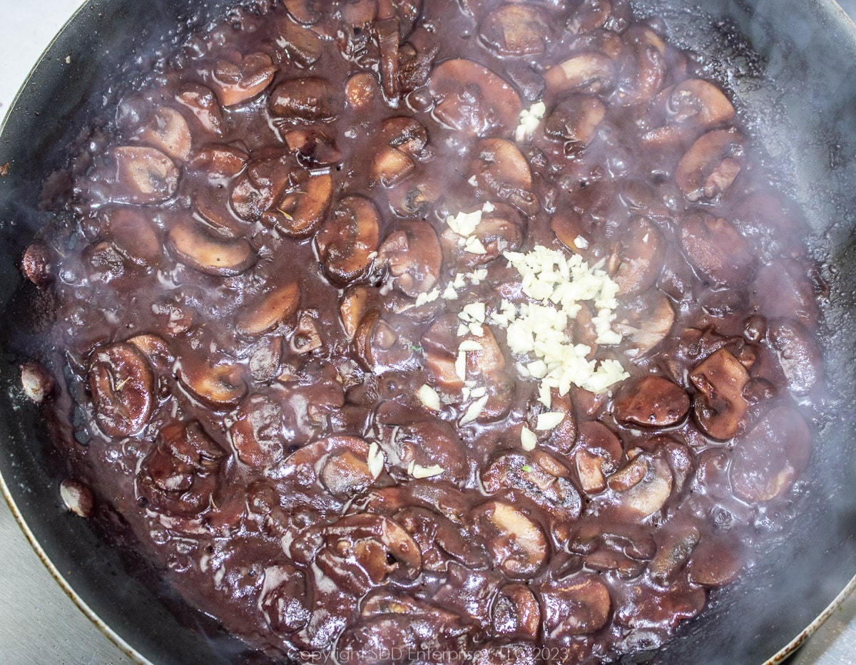 chopped garlic added to sautéed mushrooms in wine in a frying pan