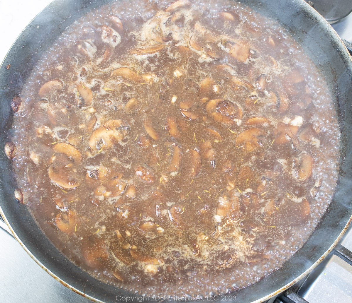 simmering mushrooms in stock and wine in a frying pan