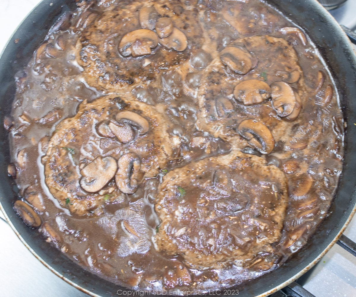 Salisbury steaks simmering in a mushroom gravy in a frying pan
