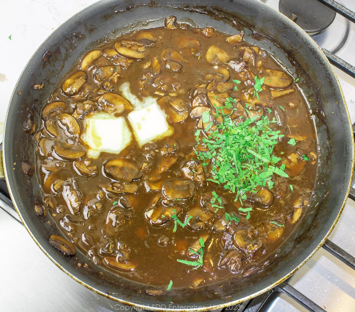 butter and parsley added to mushroom gravy in a frying pan