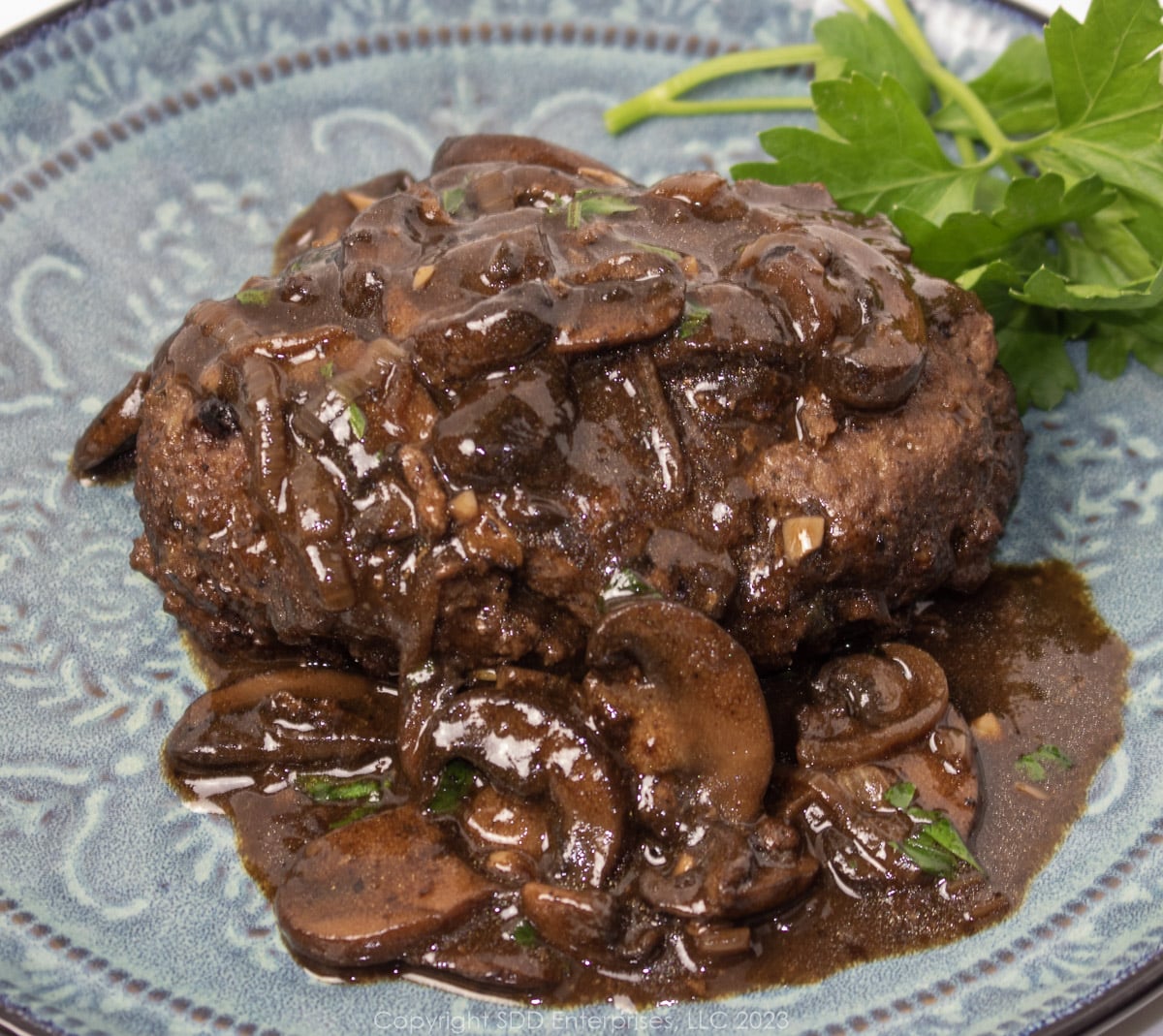 Salisbury steak with mushroom gravy and garnish on a blue green plate