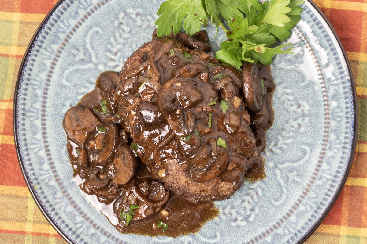 Salisbury Steak with Mushroom Gravy with garnish on a blue green plate