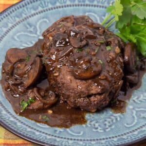 Salisbury steak with mushroom gravy and garnish on a blue green plate