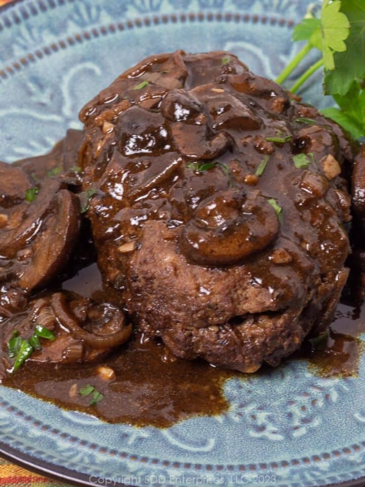 Salisbury steak with mushroom gravy and garnish on a blue green plate