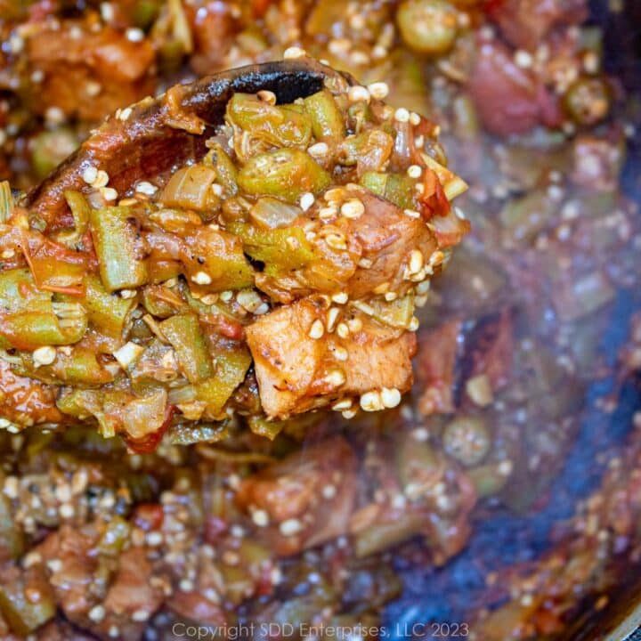 smothered okra with tomatoes and ham on a wooden spoon over a Dutch oven