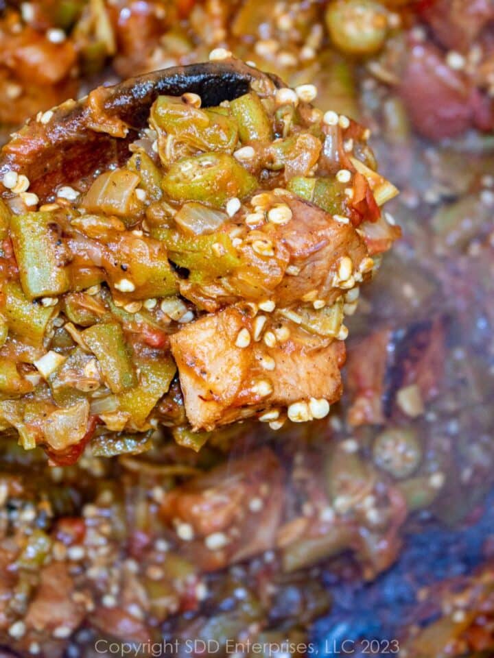 smothered okra with tomatoes and ham on a wooden spoon over a Dutch oven