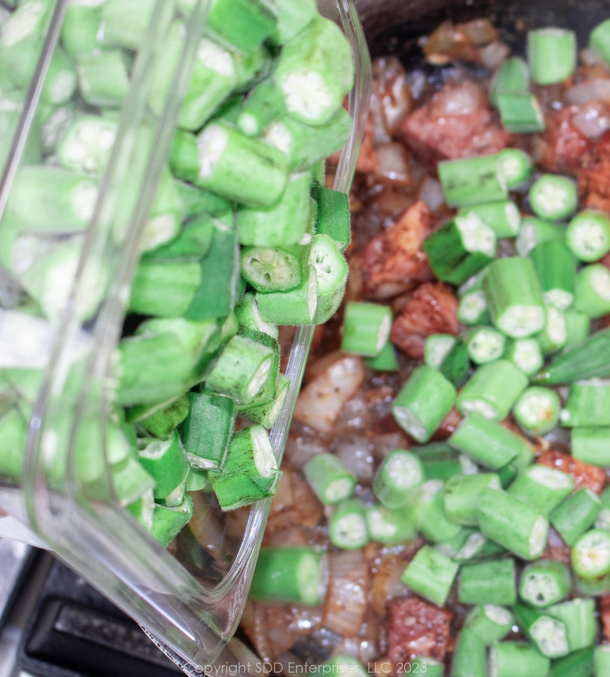 Fresh chopped okra being added to a Dutch oven