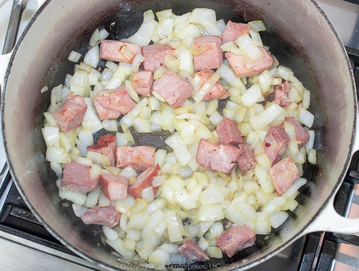 chopped yellow onions browning in a Dutch oven with ham