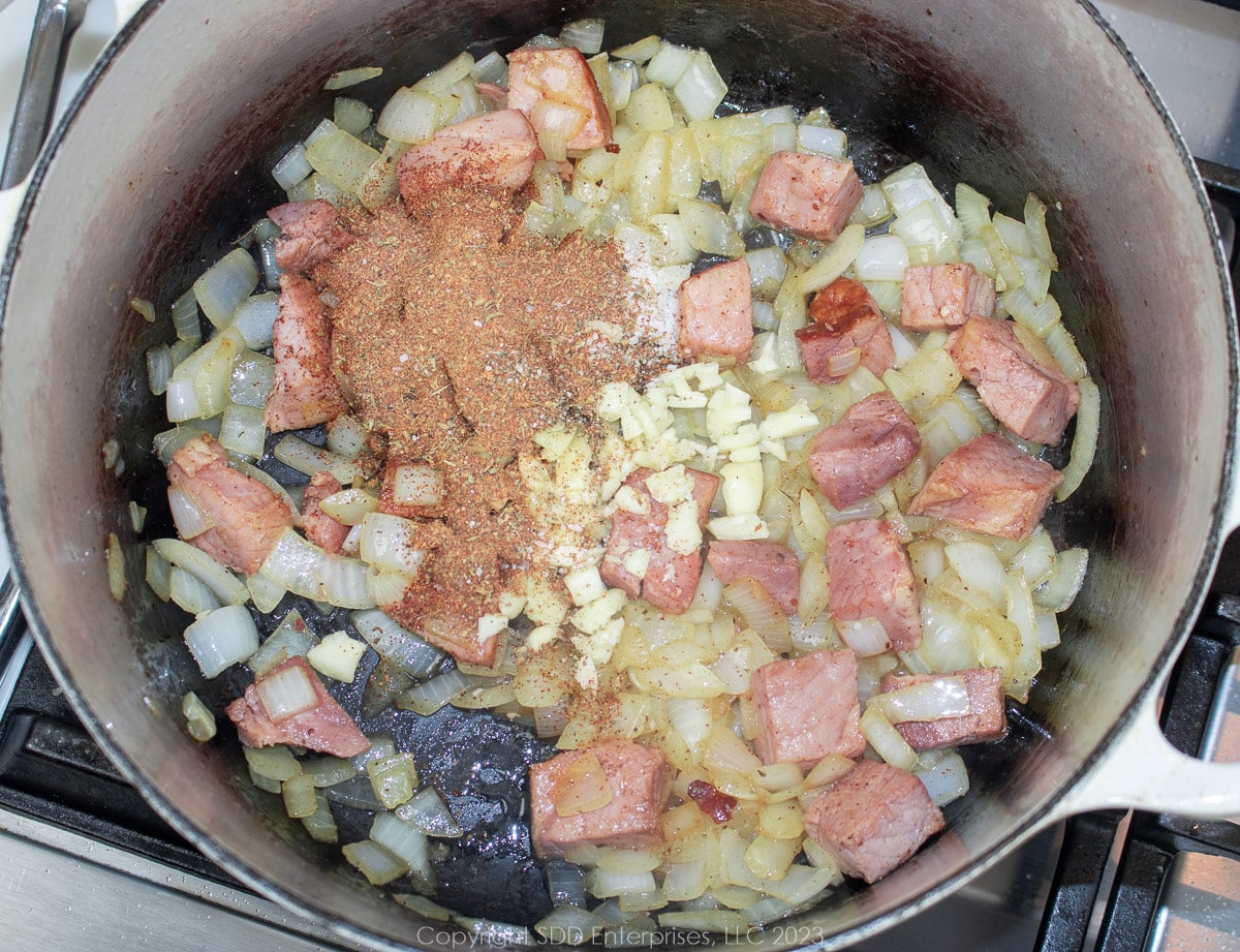 seasonings and garlic added to browning onions and ham in a Dutch oven