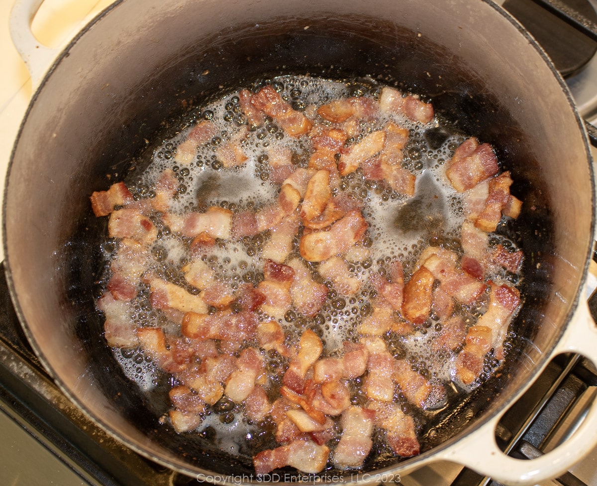 pieces of bacon frying in a Dutch oven