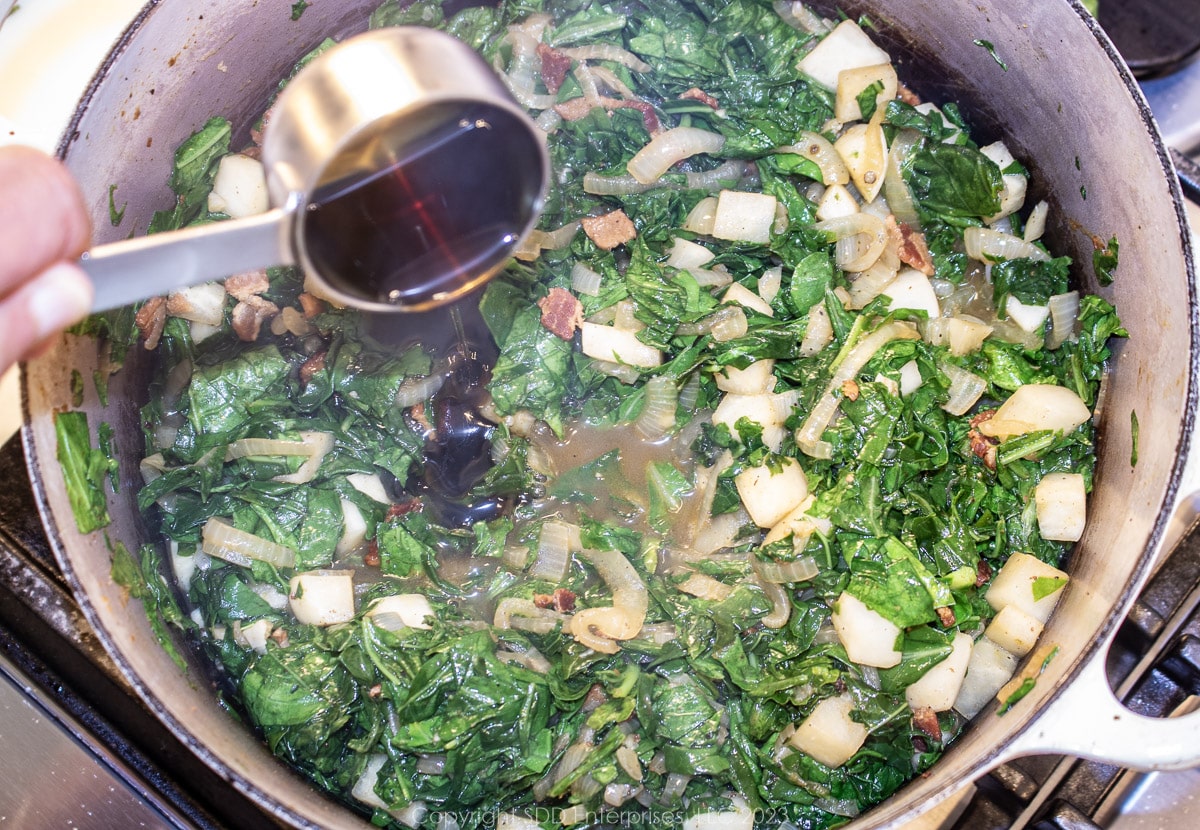 pouring cane syrup into smothering greens in a Dutch oven