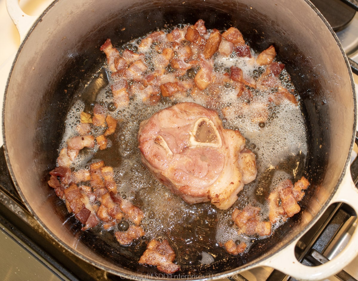 ham shank browning with bacon in a Dutch oven