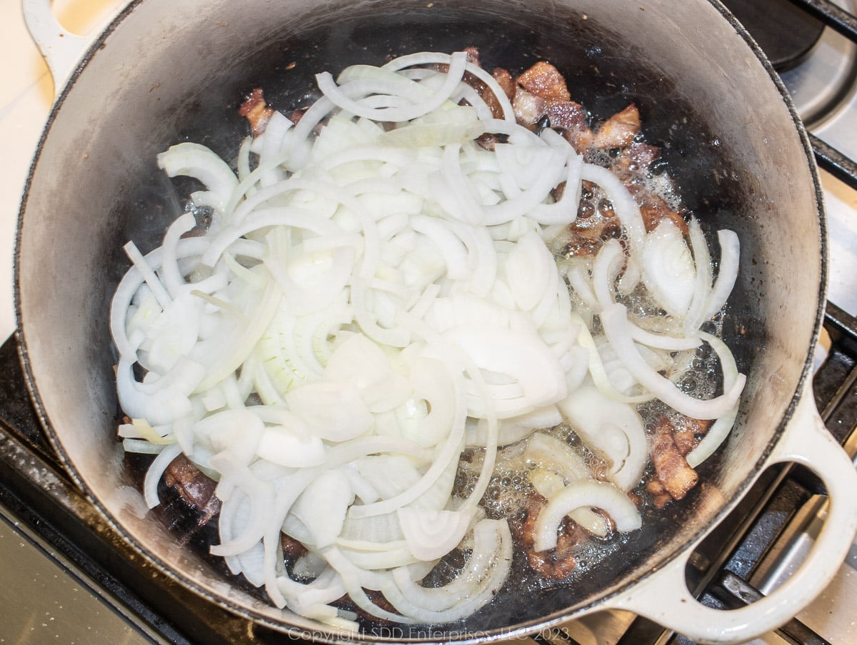 sliced onions sautéing in a Dutch oven with ham and bacon