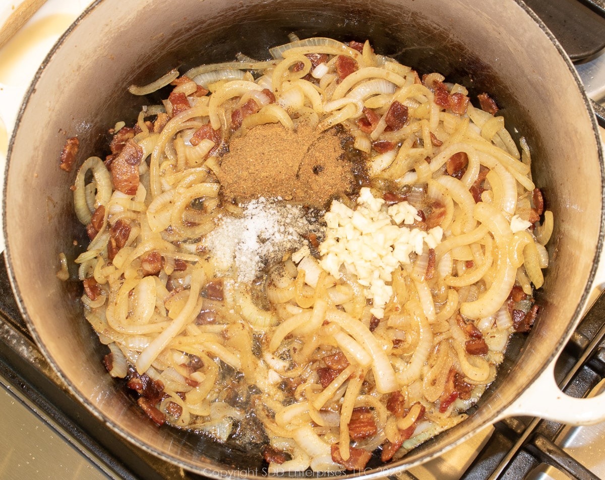 garlic, herbs and spices and creole seasoning added to sautéed onions in a Dutch oven