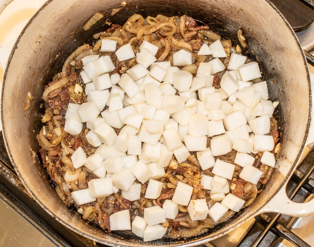 cubed turnips with sautéed onions and ham and bacon in a Dutch oven