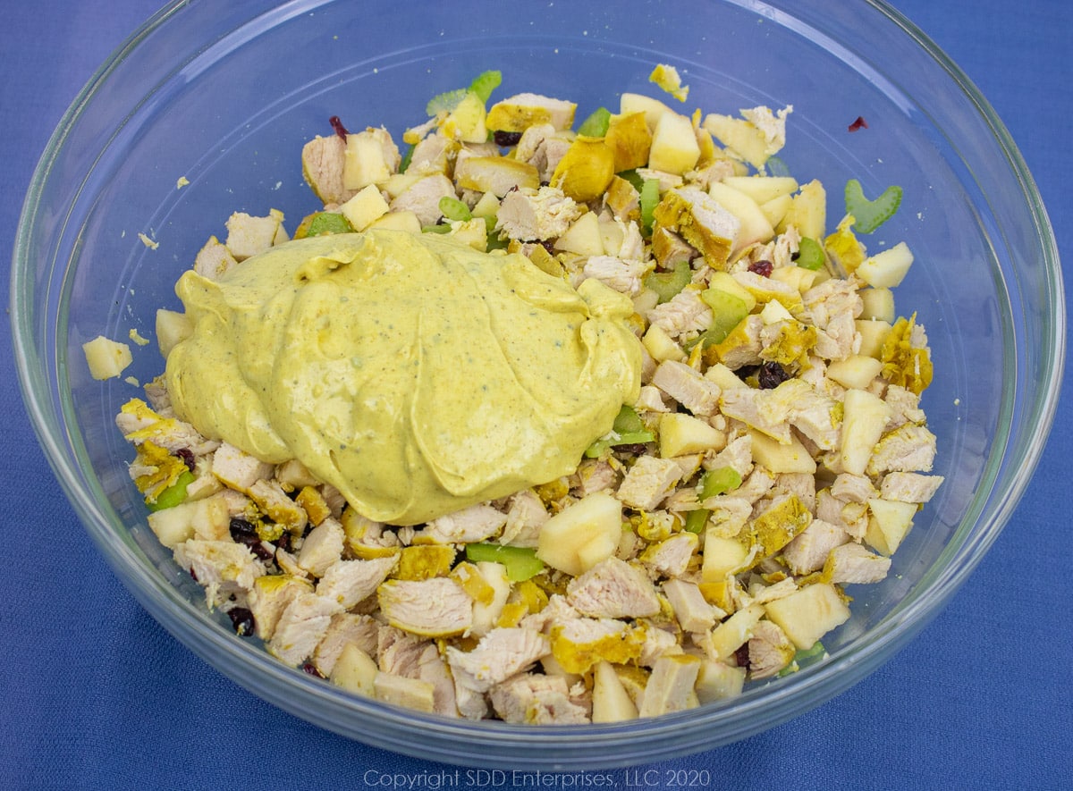 Mixed chicken breasts and fruit and veggie with lemon curry dressing in a glass bowl