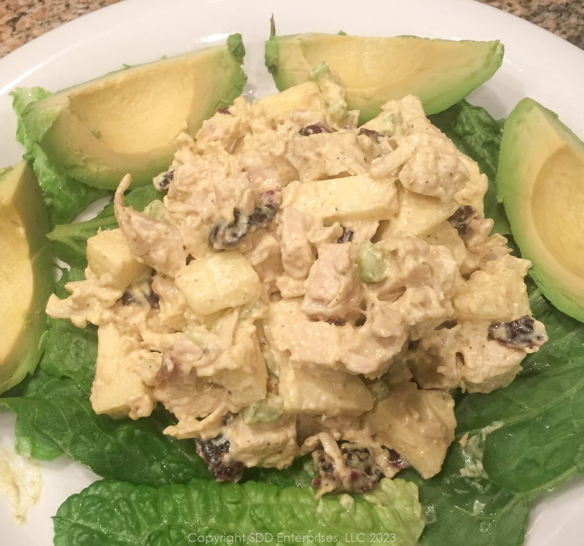 curry chicken salad with cranberries and apples on a bed of lettuce with avocado slices on a plate