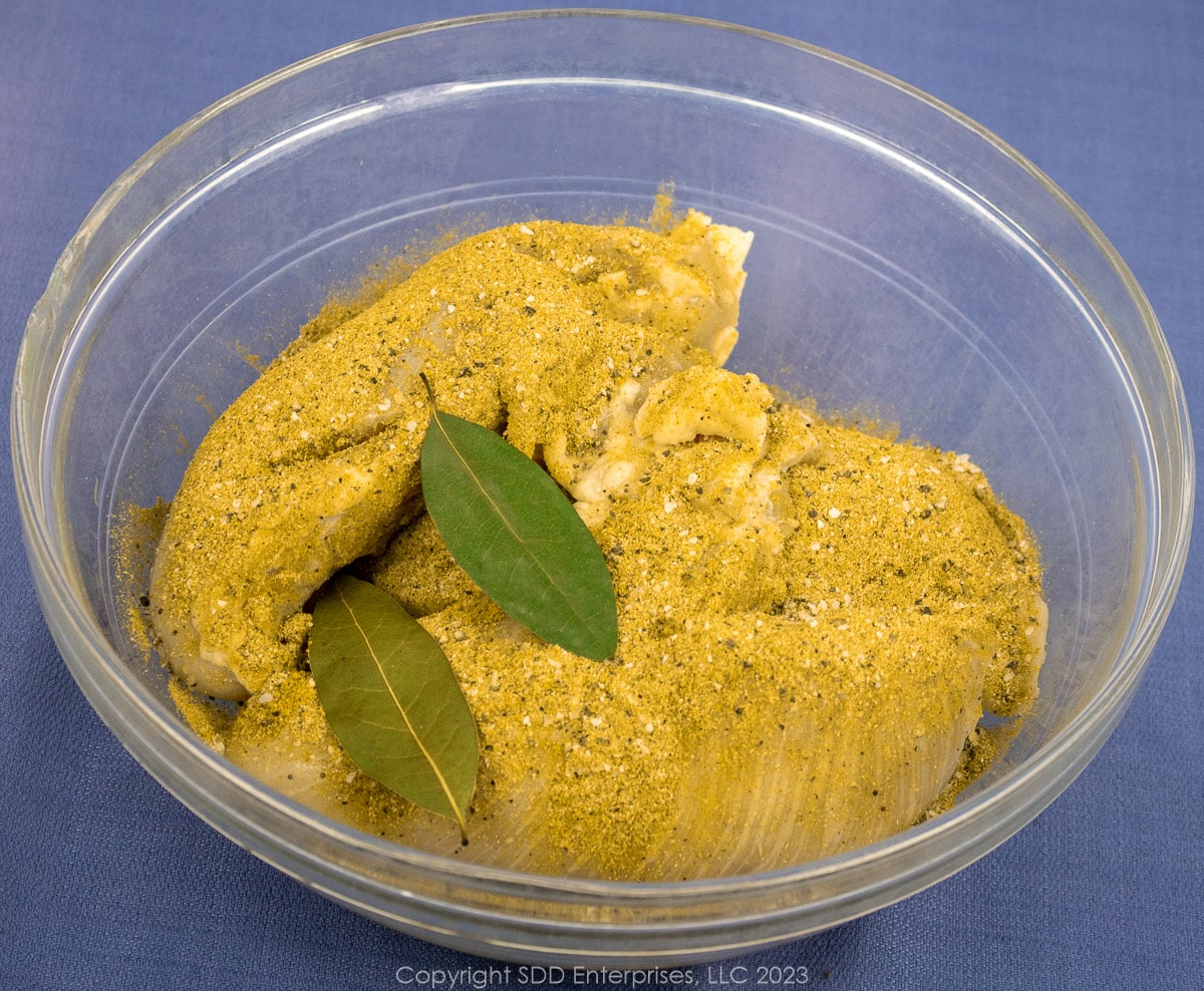 chicken breasts seasoned with spices and bay leaves in a glass bowl