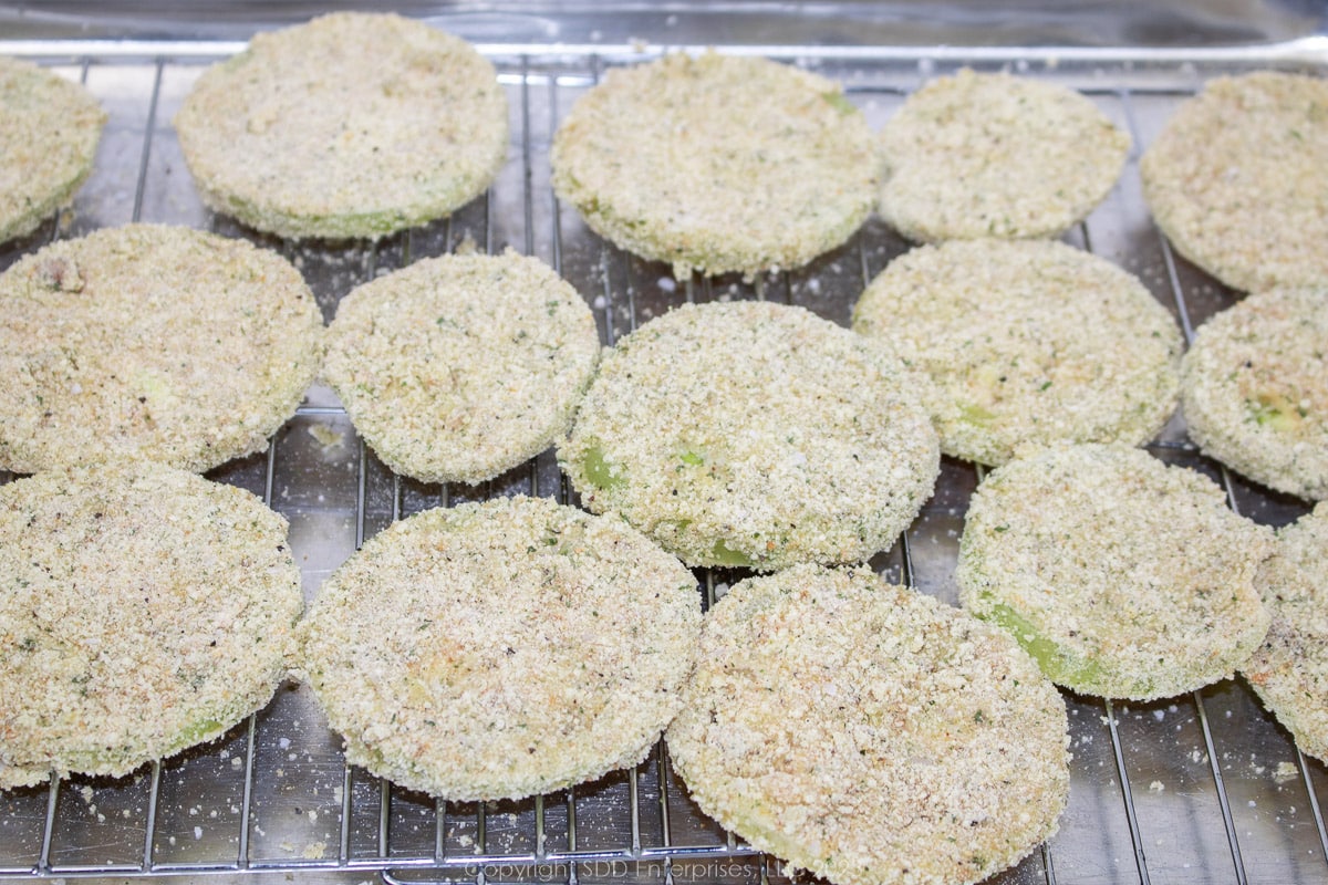breaded slices of green tomatoes on a rack ready for the fryer