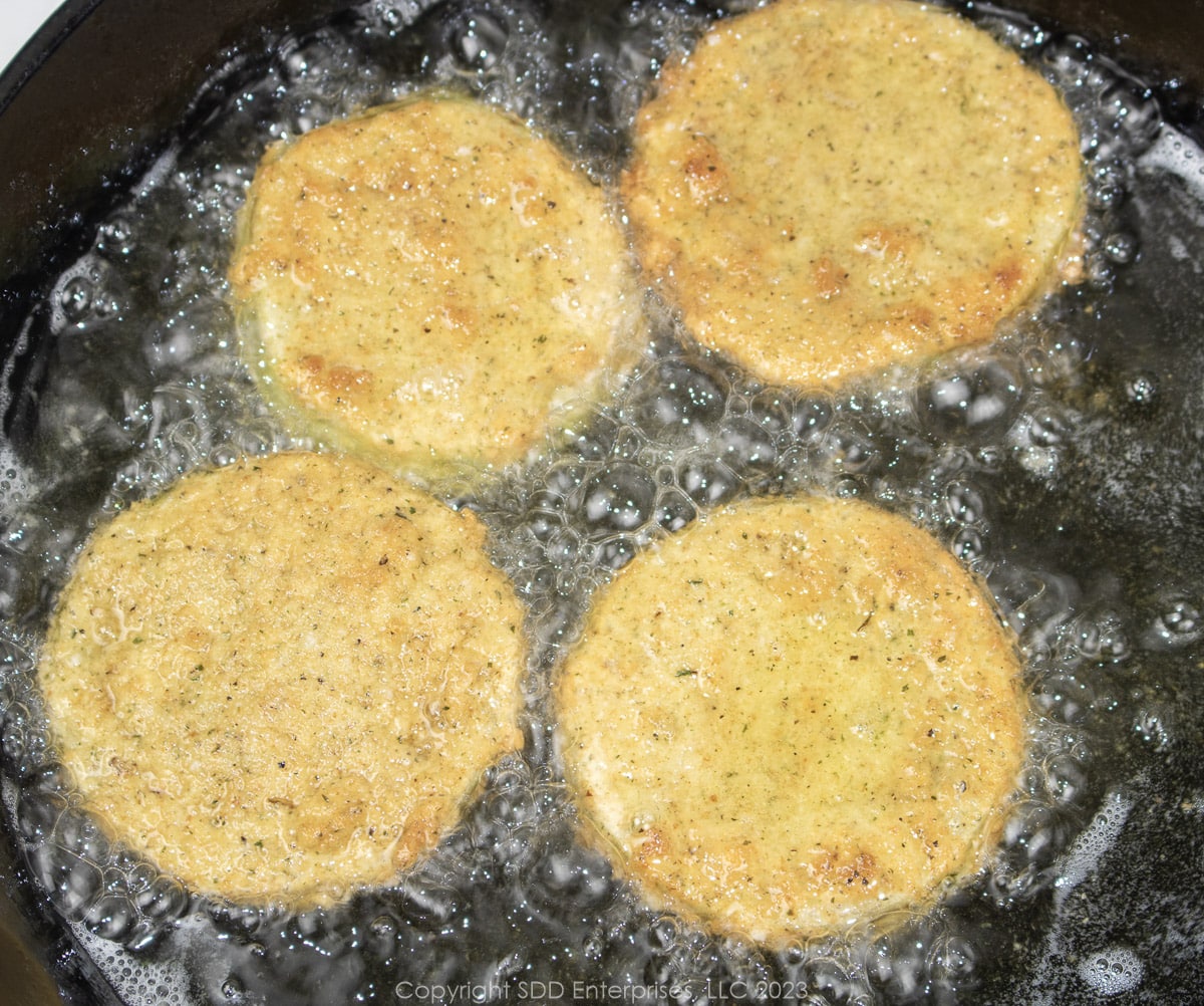 four slices of breaded green tomatoes frying in oil