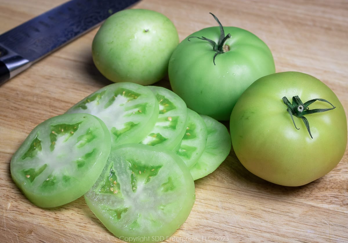 Sliced and whole green tomatoes on a cutting board with a chef's knife