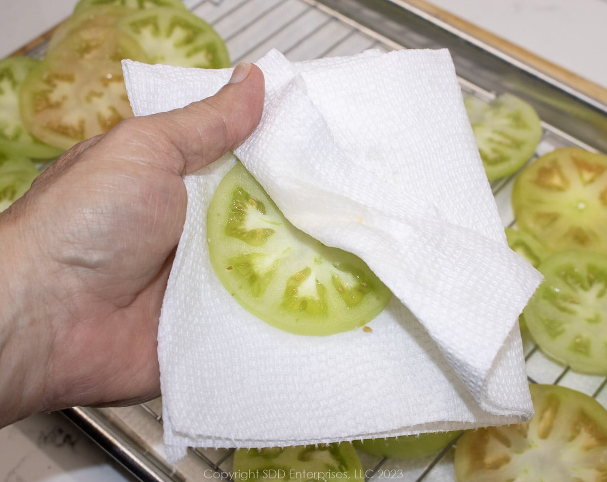 slice of green tomato being patted dry with paper towel