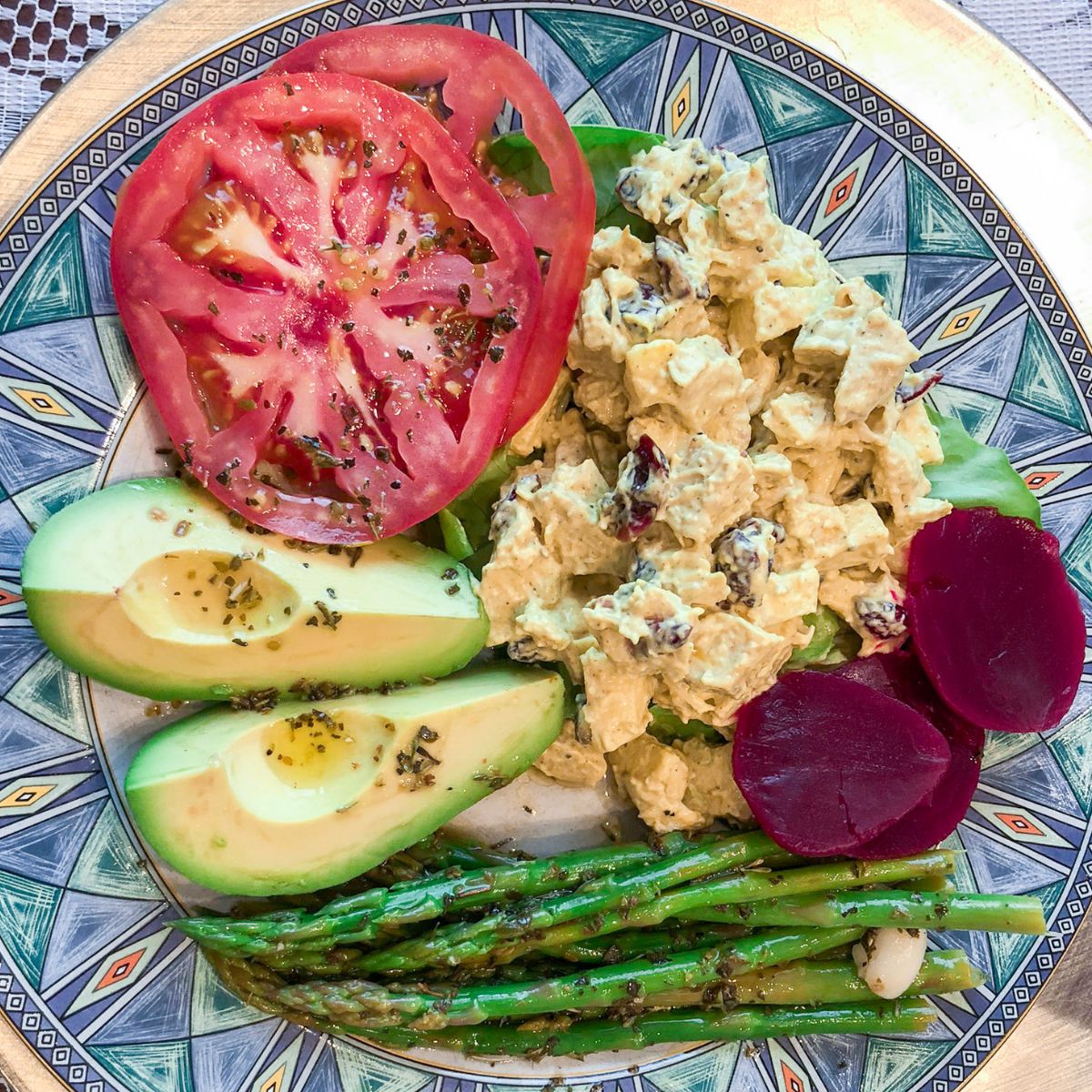 a plate with chicken salad, tomatoes, beets, asparagus and avocado slices