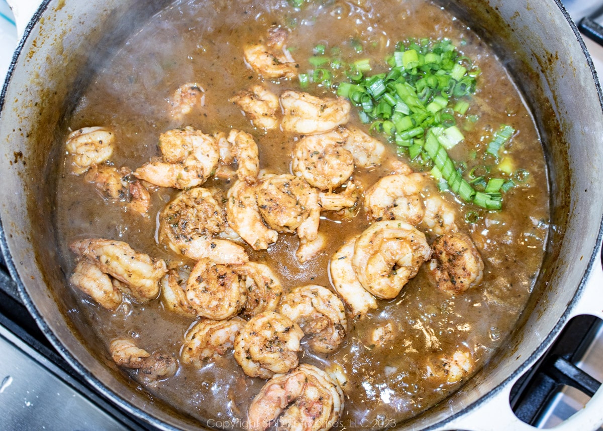 shrimp and green onions added to a gravy in a Dutch oven