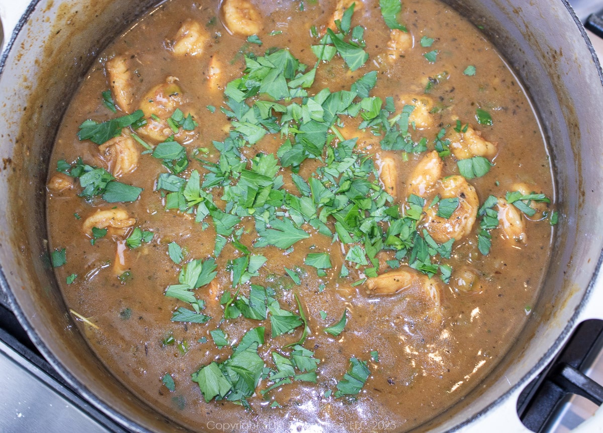 chopped parsley added to shrimp étouffée in a Dutch oven