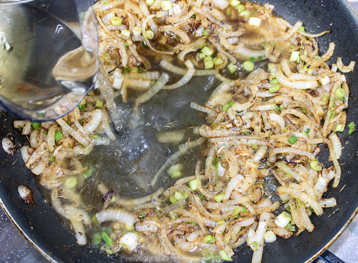 liquids being added to sautéed onions in a fry pan